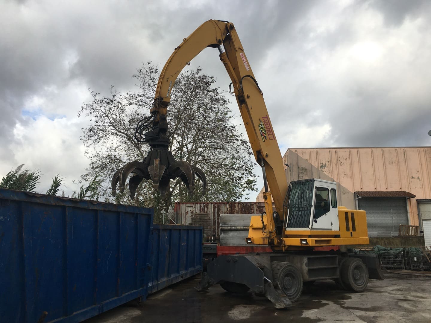 Gru a polipo che carica rottami metallici in un cassone nel piazzale dell'autodemolizione
